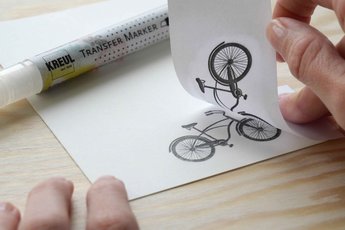 Hand mit Postkarte auf die ein Fahrrad-Motiv mit Marker übertragen wird