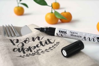 Stoffserviette wird mit einem schwarzen Textil Stift beschriftet Orangen im Hintergrund