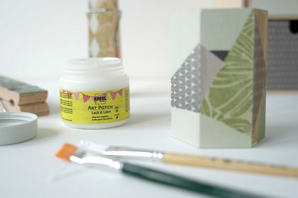 Dose mit KREUL Art Potch, Pinsel, Serviette und mit Serviette beklebte Ordnungshelfer auf einem Tisch