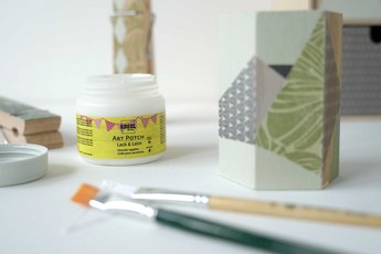 Dose mit KREUL Art Potch, Pinsel, Serviette und mit Serviette beklebte Ordnungshelfer auf einem Tisch